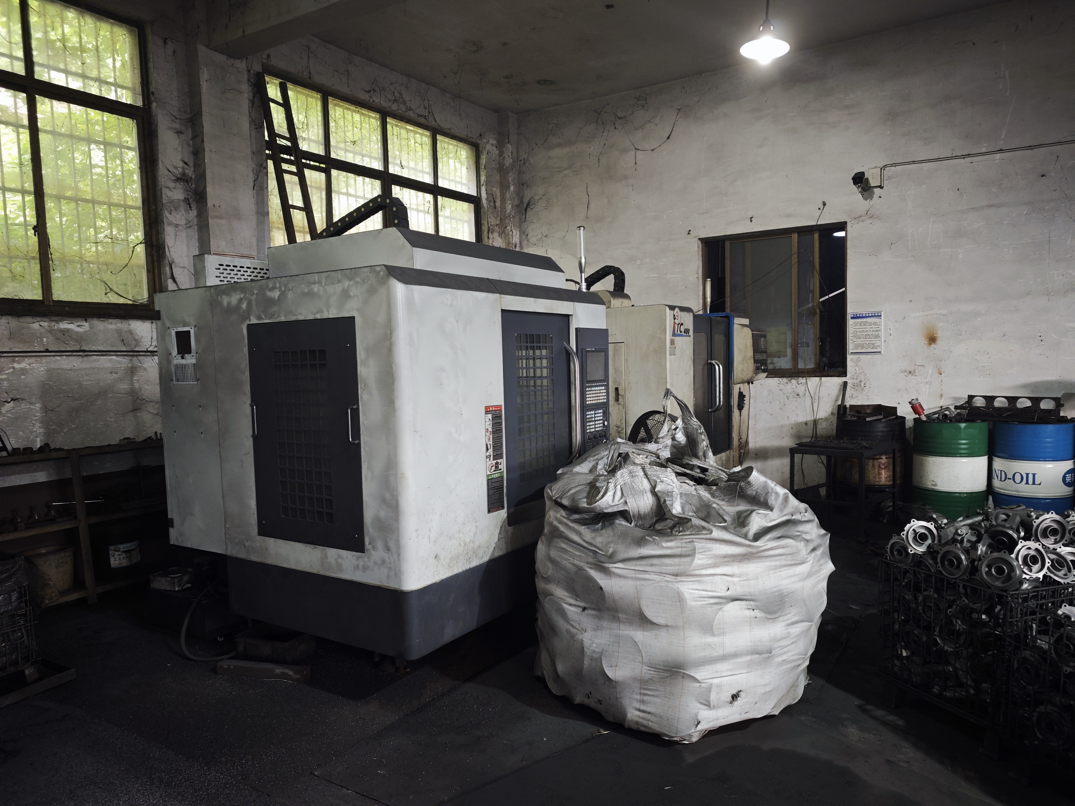 A CNC machining centre with a large bulk bag beside it and a wire-mesh basket of cast parts on the right